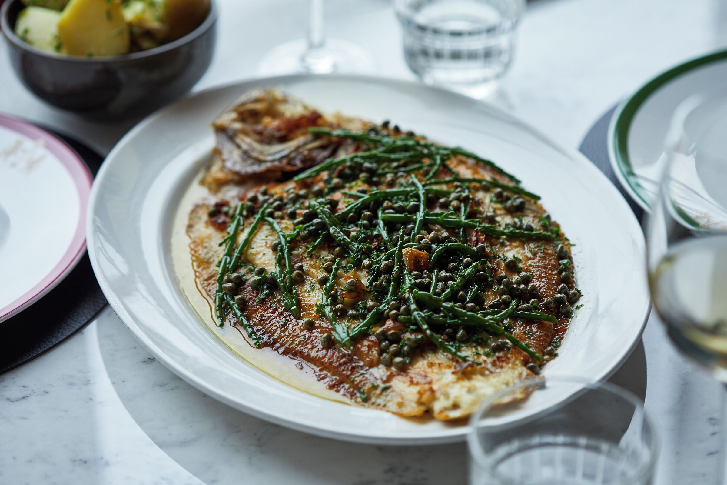 A plate of food with greens and capers on a white plate.