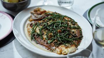 A plate of food with greens and capers on a white plate.
