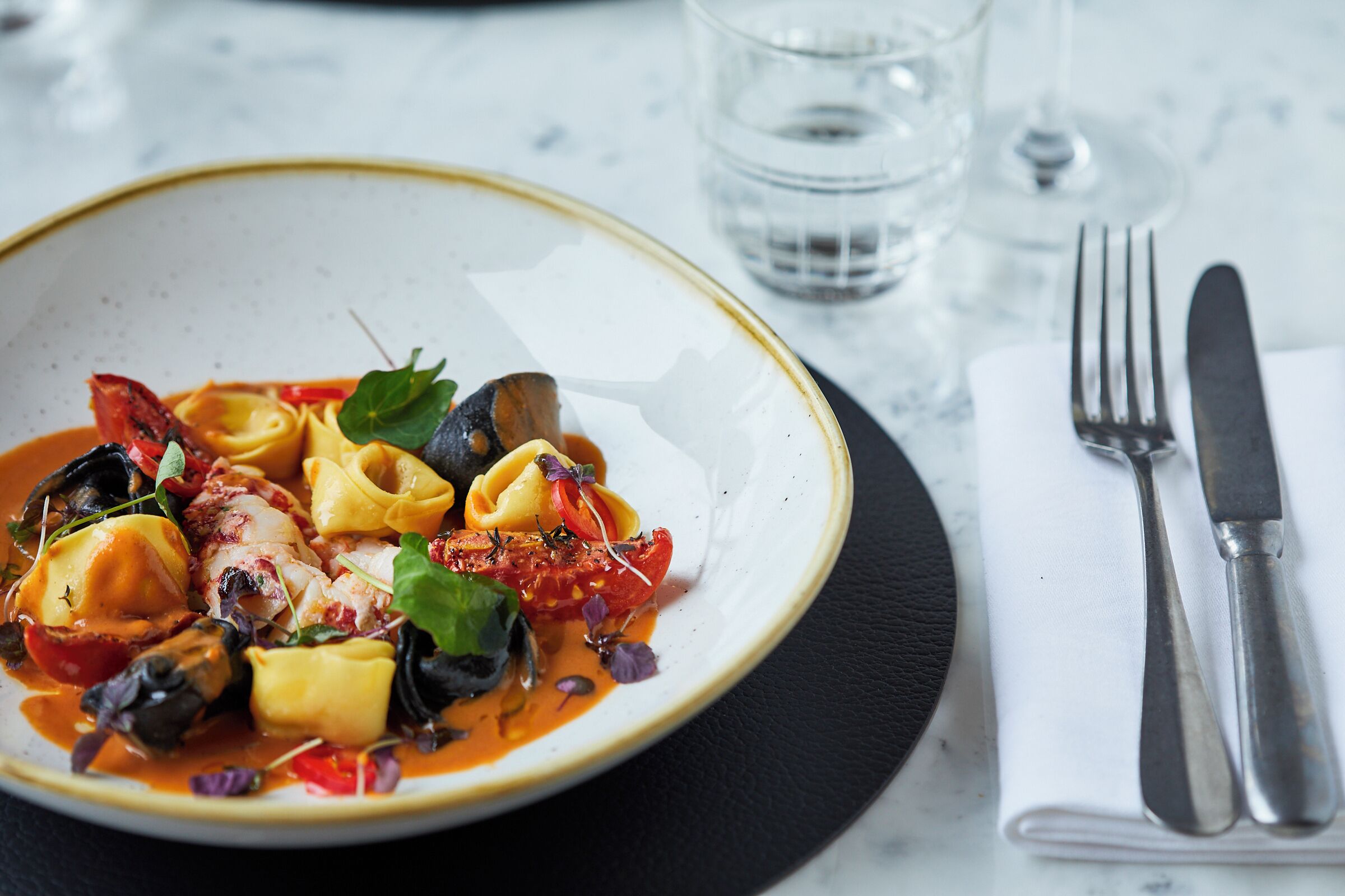 A plate of pasta with a tomato-based sauce, garnished with herbs and vegetables.