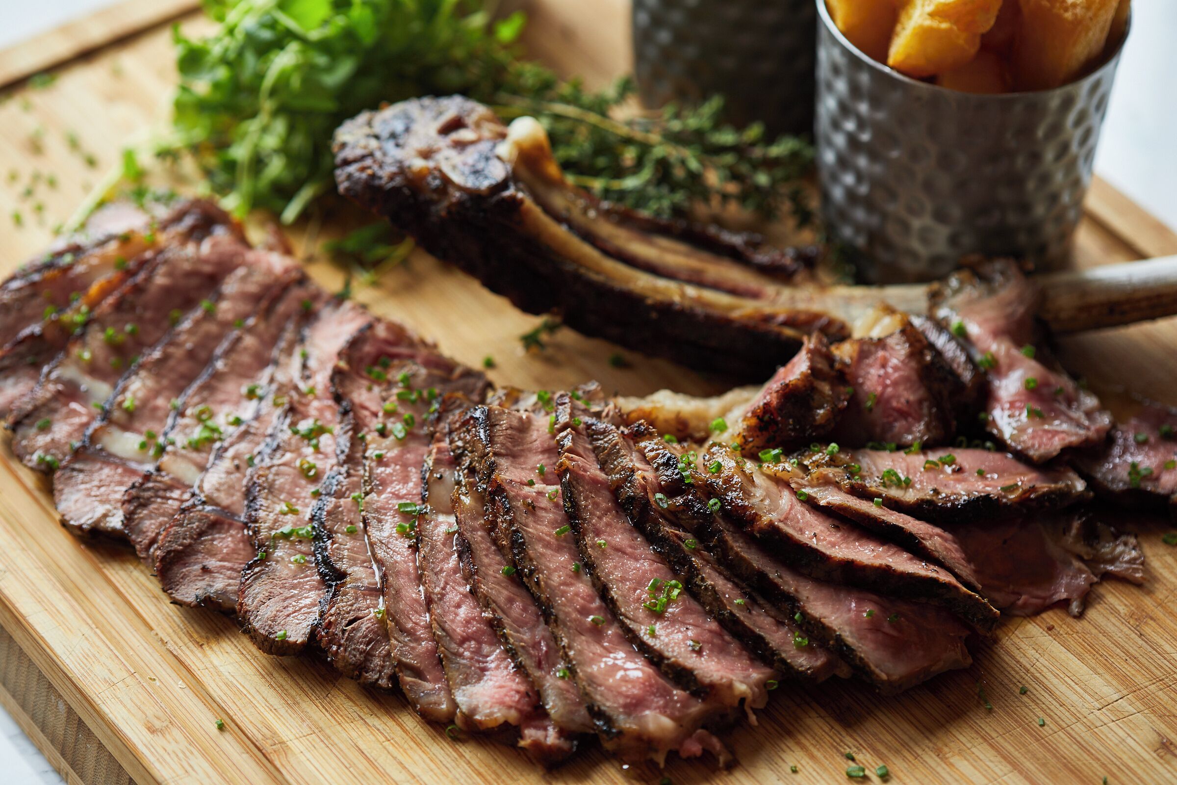 A wooden cutting board with sliced steak and mushrooms, garnished with herbs.