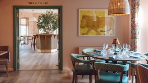 Un comedor con una mesa redonda dispuesta para cuatro personas, sillas con tapicería estampada, una lámpara colgante y un cuadro abstracto de gran tamaño en la pared.