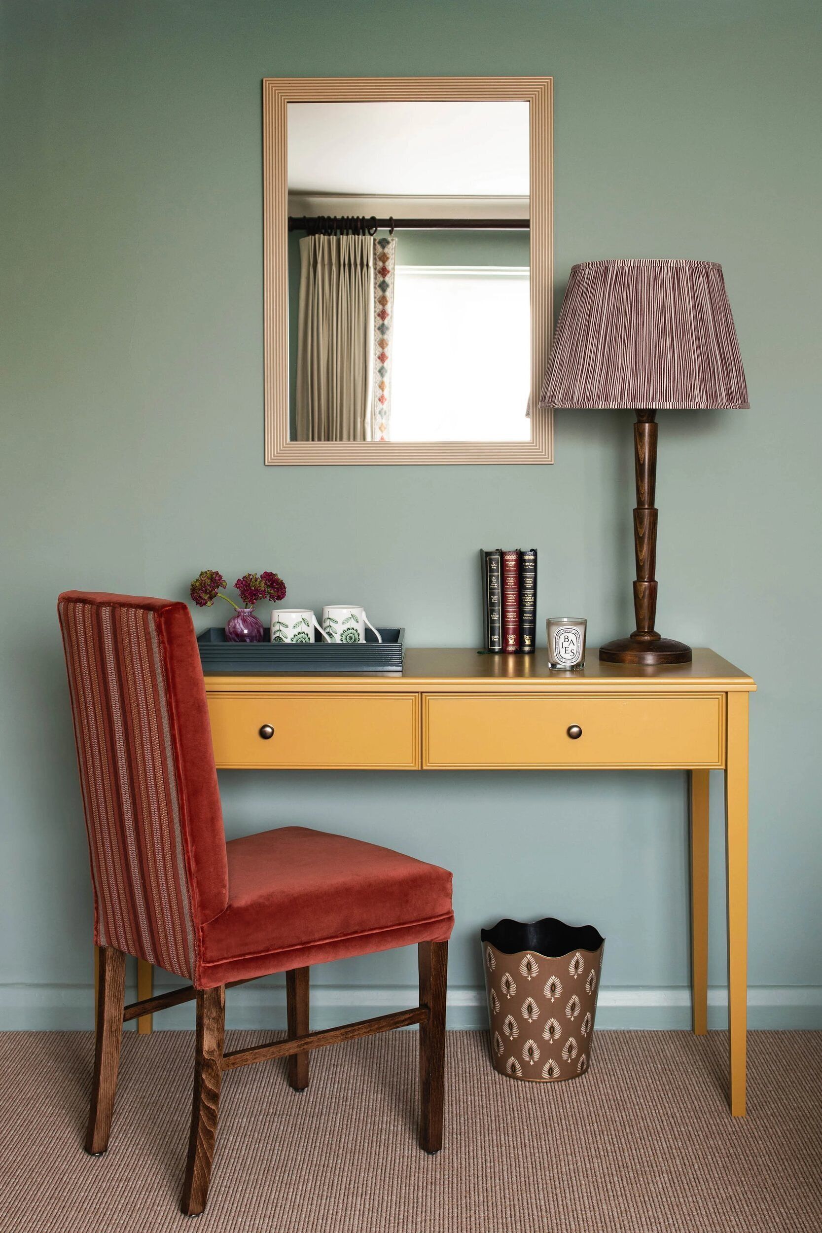 A desk with a mirror, a lamp, and decorative items.