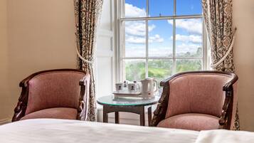 Una habitación con dos sillones tapizados, una mesa de vidrio con juego de té, y un ventanal con vistas a la vegetación.
