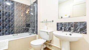 Un baño con bañera, inodoro y lavamanos, todo con azulejos de mármol.