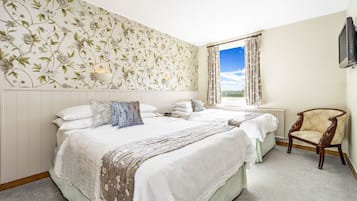 A hotel room with two beds, a large window with curtains, a wooden chair, and a wall-mounted TV.