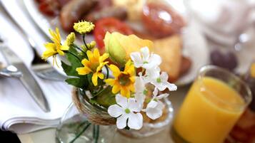 A table with a glass of orange juice, a small vase with white and yellow flowers, and a plate of food.