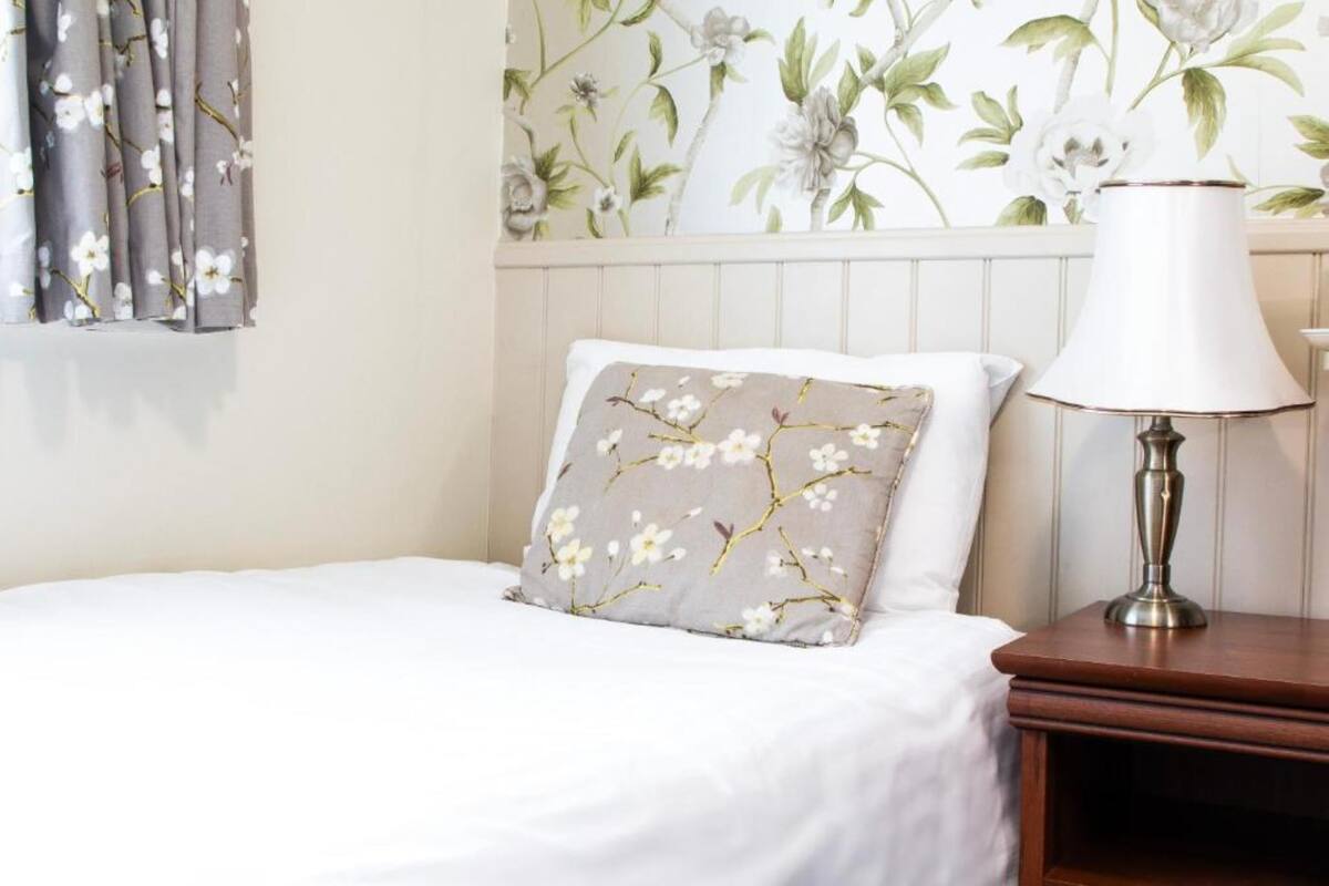Un lit avec un coussin à motifs floraux, une lampe de chevet et un papier peint à fleurs.