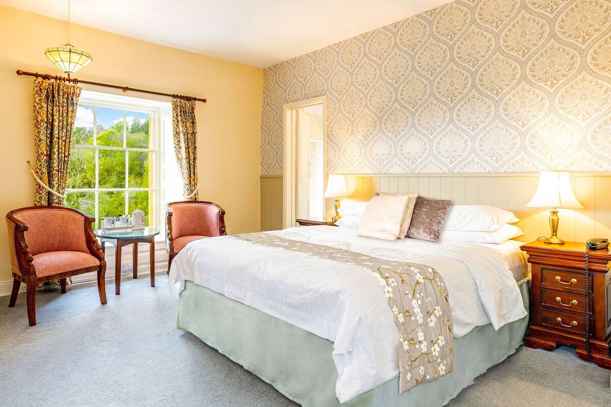 Une chambre à coucher avec un grand lit, deux chaises, une petite table et une table de chevet avec des lampes.