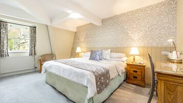 A bedroom with a large bed, two bedside tables with lamps, a chair, a desk, and a patterned wallpaper.