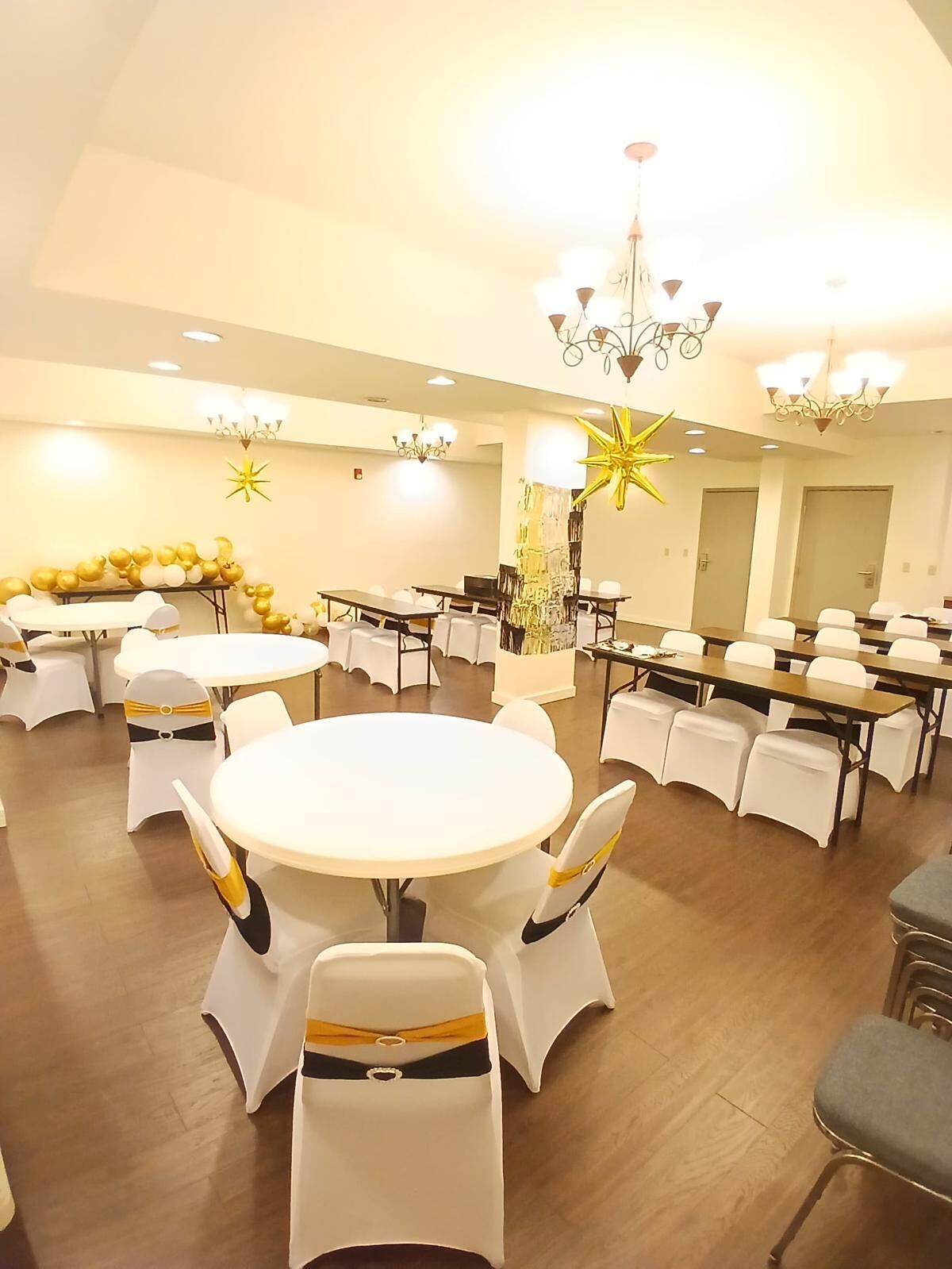 Un salón de banquetes con mesas redondas y sillas blancas, candelabros y decoraciones doradas.