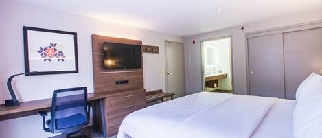 Une chambre d’hôtel avec un lit, un bureau et une chaise, une télévision et un tableau encadré au mur.
