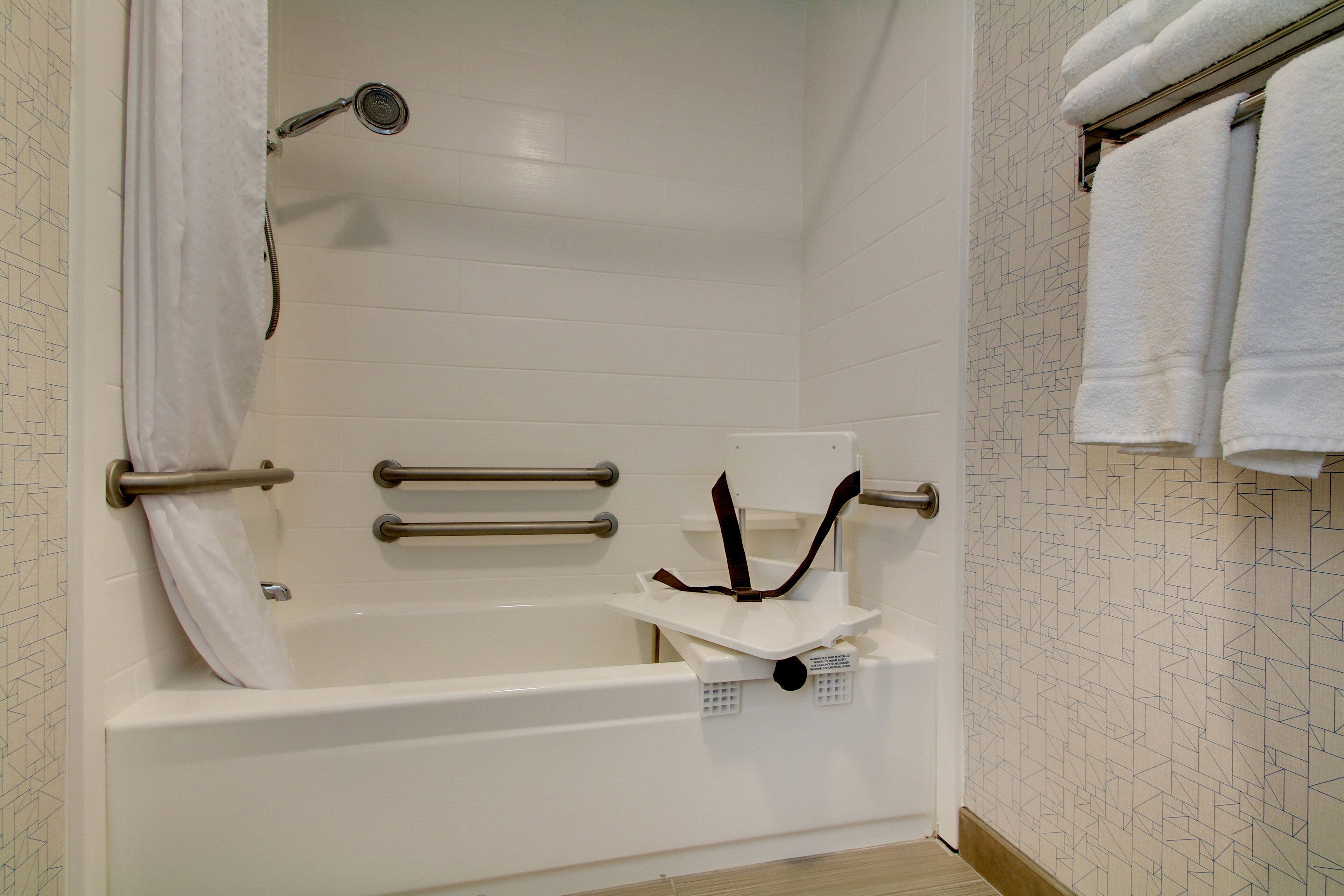 Una bañera blanca con barras de apoyo, un cabezal de ducha y un perchero para toallas.