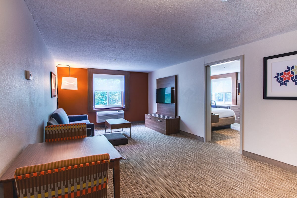 Ein modernes Hotelzimmer mit einer Couch, einem Esstisch, einem Fernseher und einem Bett.