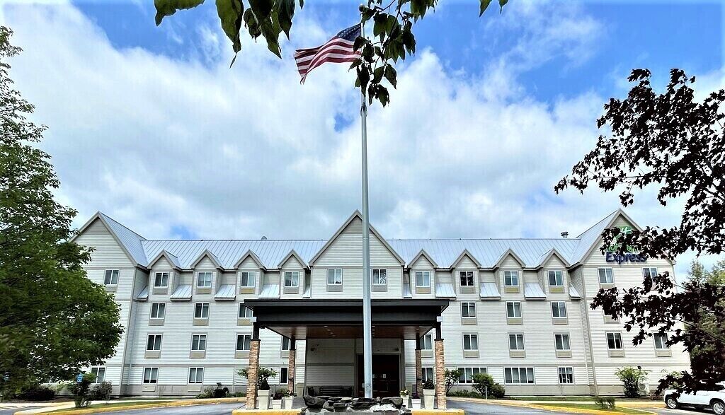 A multi-story hotel with a central entrance, a flagpole with an American flag, and a covered parking area.