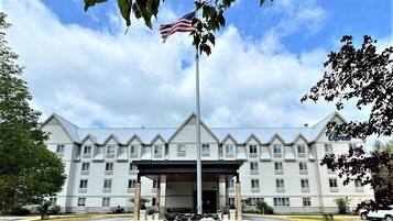 A multi-story hotel with a central entrance, a flagpole with an American flag, and a covered parking area.