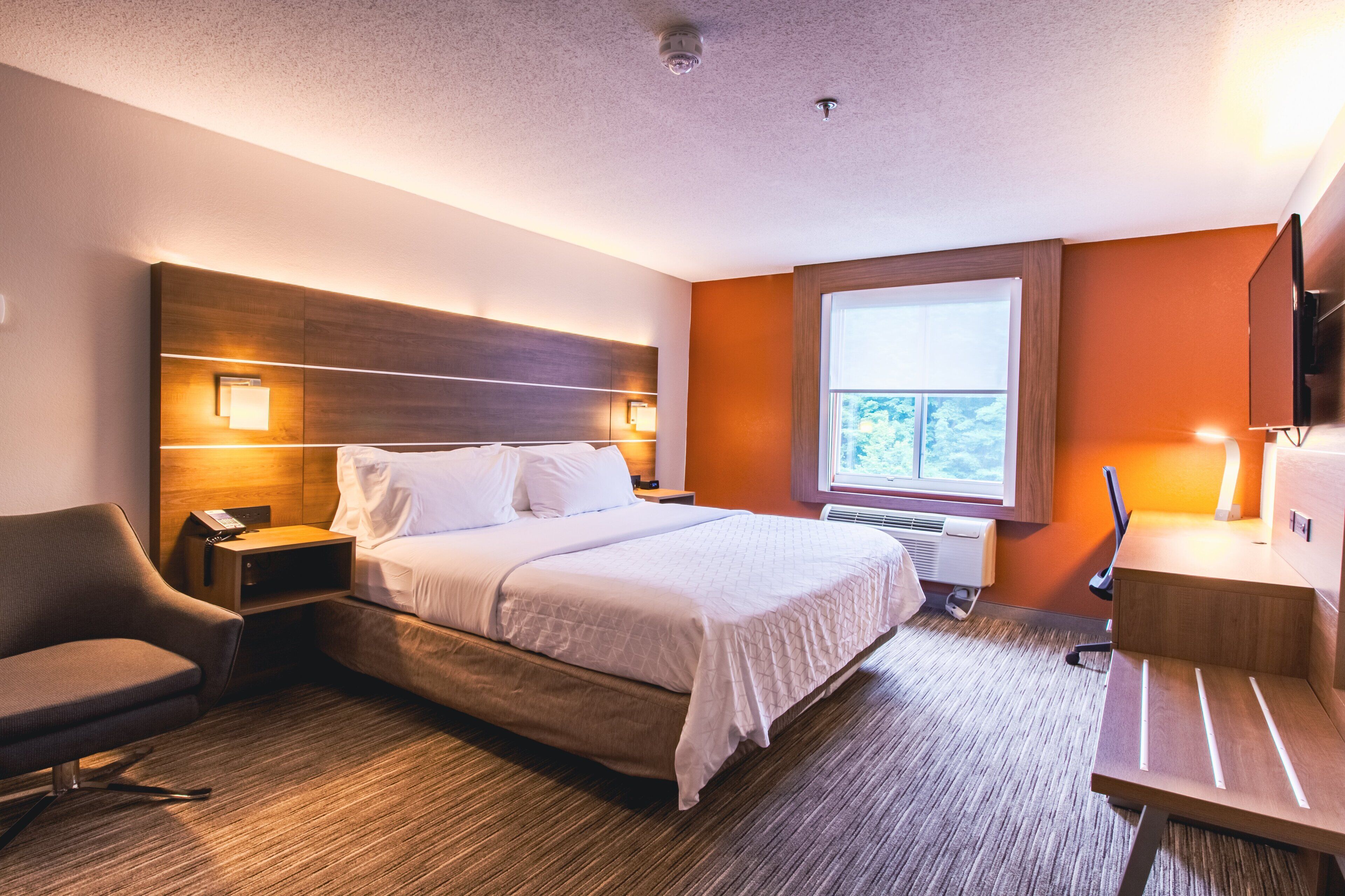 A hotel room with a large bed, bedside lamps, a desk with a chair, and a TV.