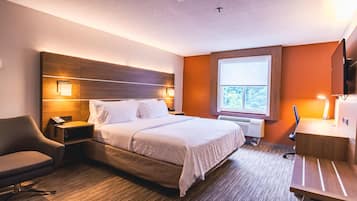 A hotel room with a large bed, bedside lamps, a desk with a chair, and a TV.