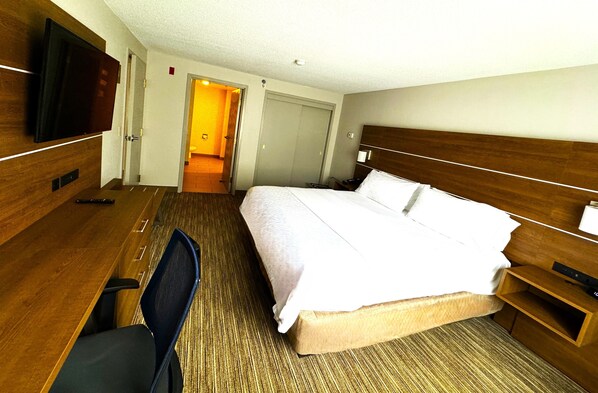 A hotel room with a bed, a desk, a chair, a TV, and a wooden headboard.