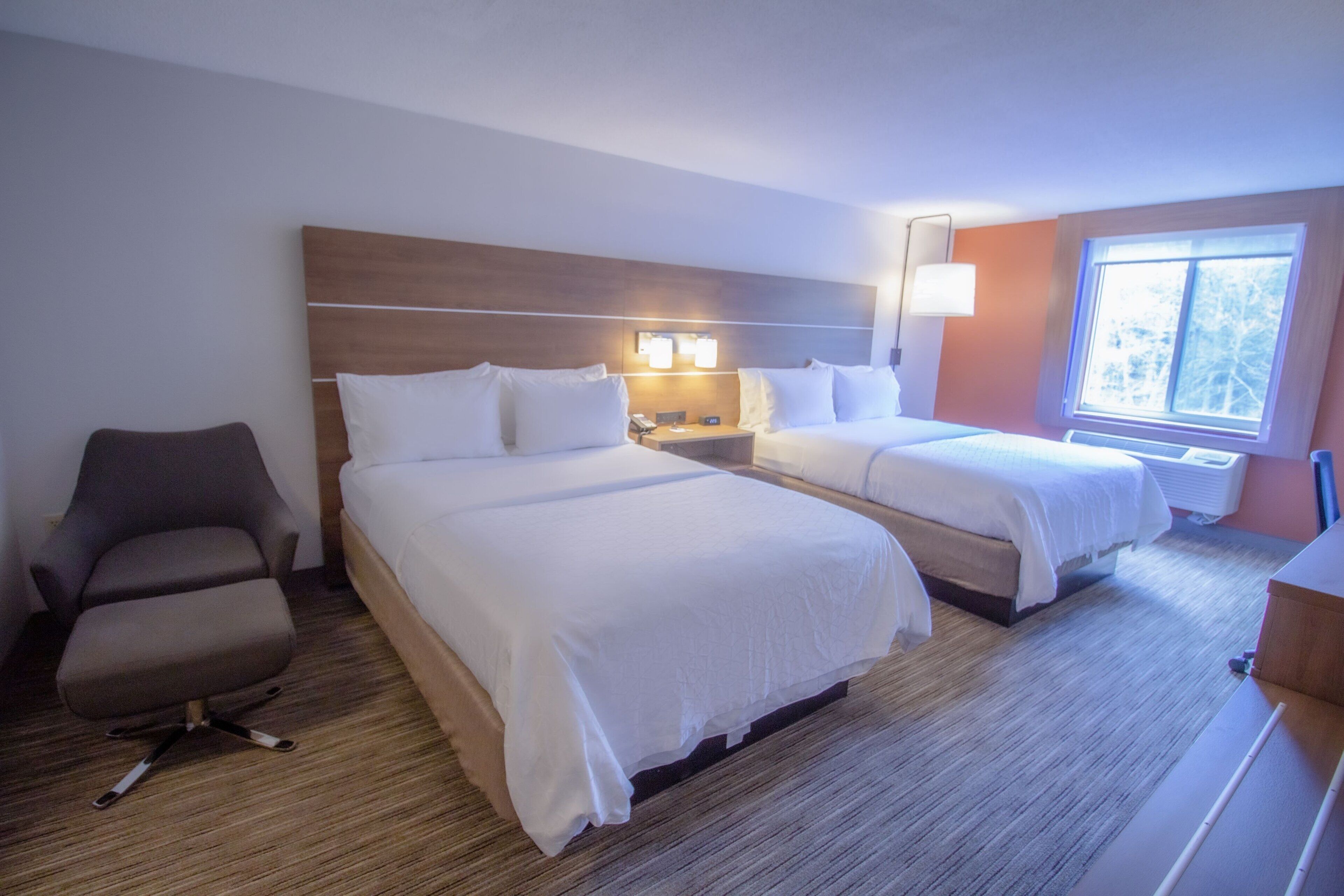 A hotel room with two beds, a desk, a chair, and a window with a view.