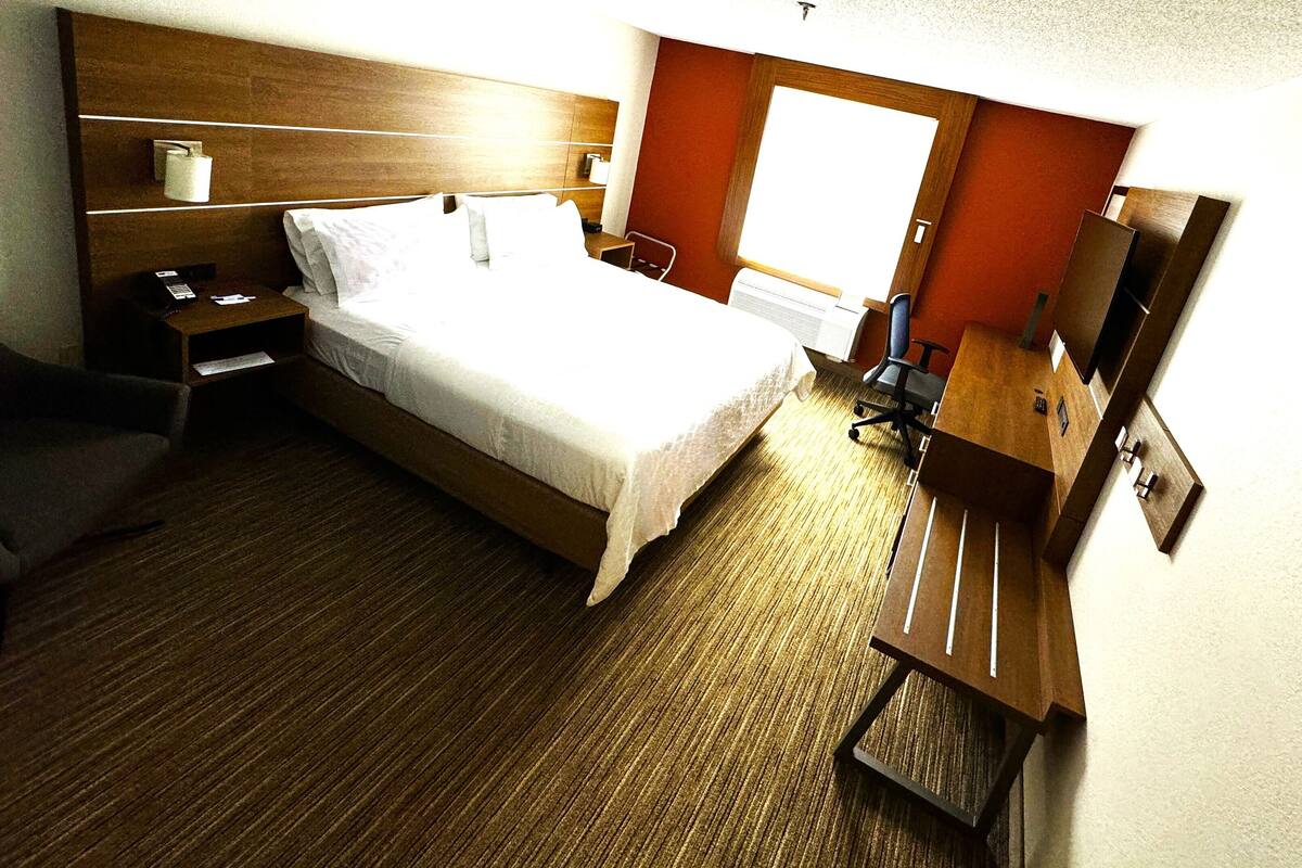 Ein Hotelzimmer mit Bett, Nachttisch, Sessel, Schreibtisch und einem kleinen Fernseher.