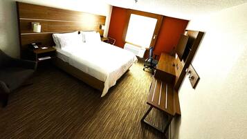 Ein Hotelzimmer mit Bett, Nachttisch, Sessel, Schreibtisch und einem kleinen Fernseher.