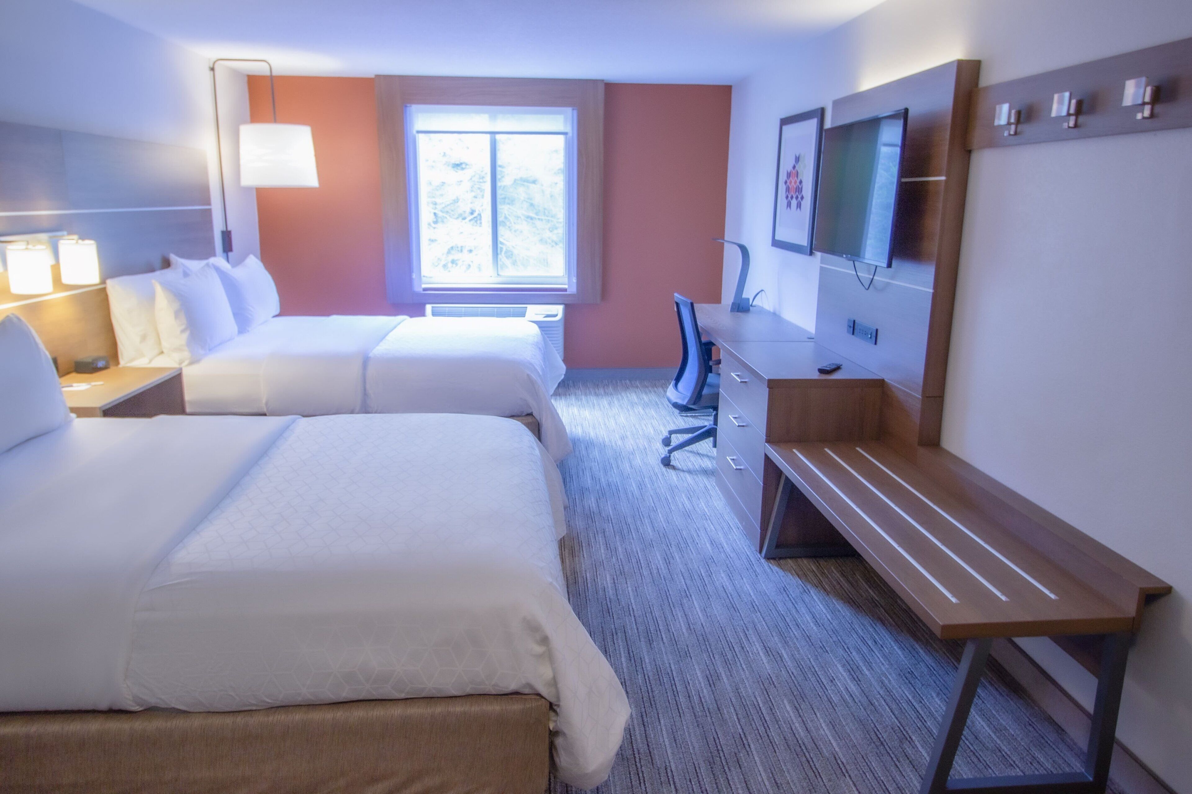 A hotel room with two beds, a desk, a chair, a TV, and a window with a view.
