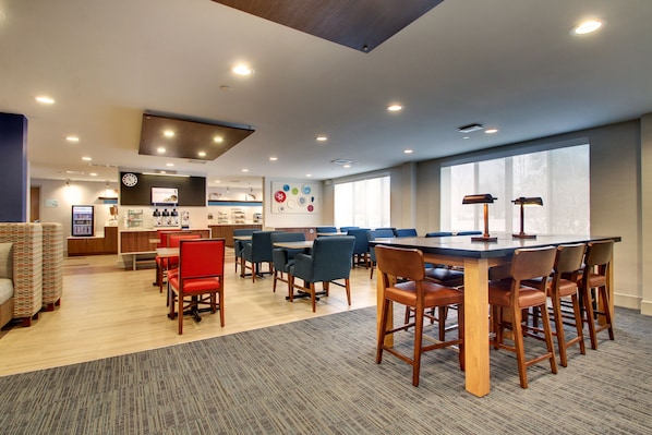 A modern hotel lobby with a large dining area, a reception desk, and a clock on the wall.