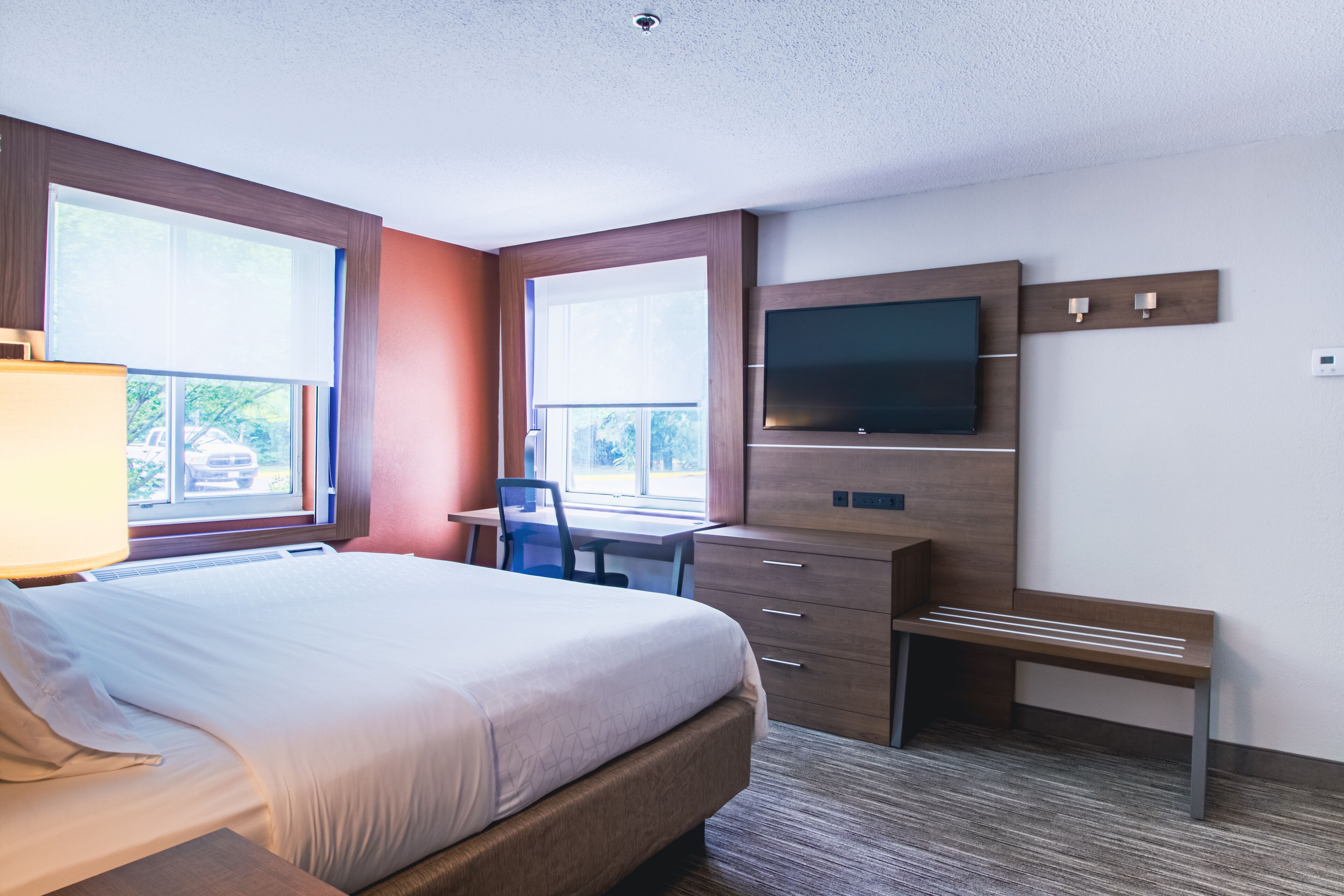 Une chambre d’hôtel équipée d’un lit, d’un bureau, d’une chaise, d’une télévision et de fenêtres.