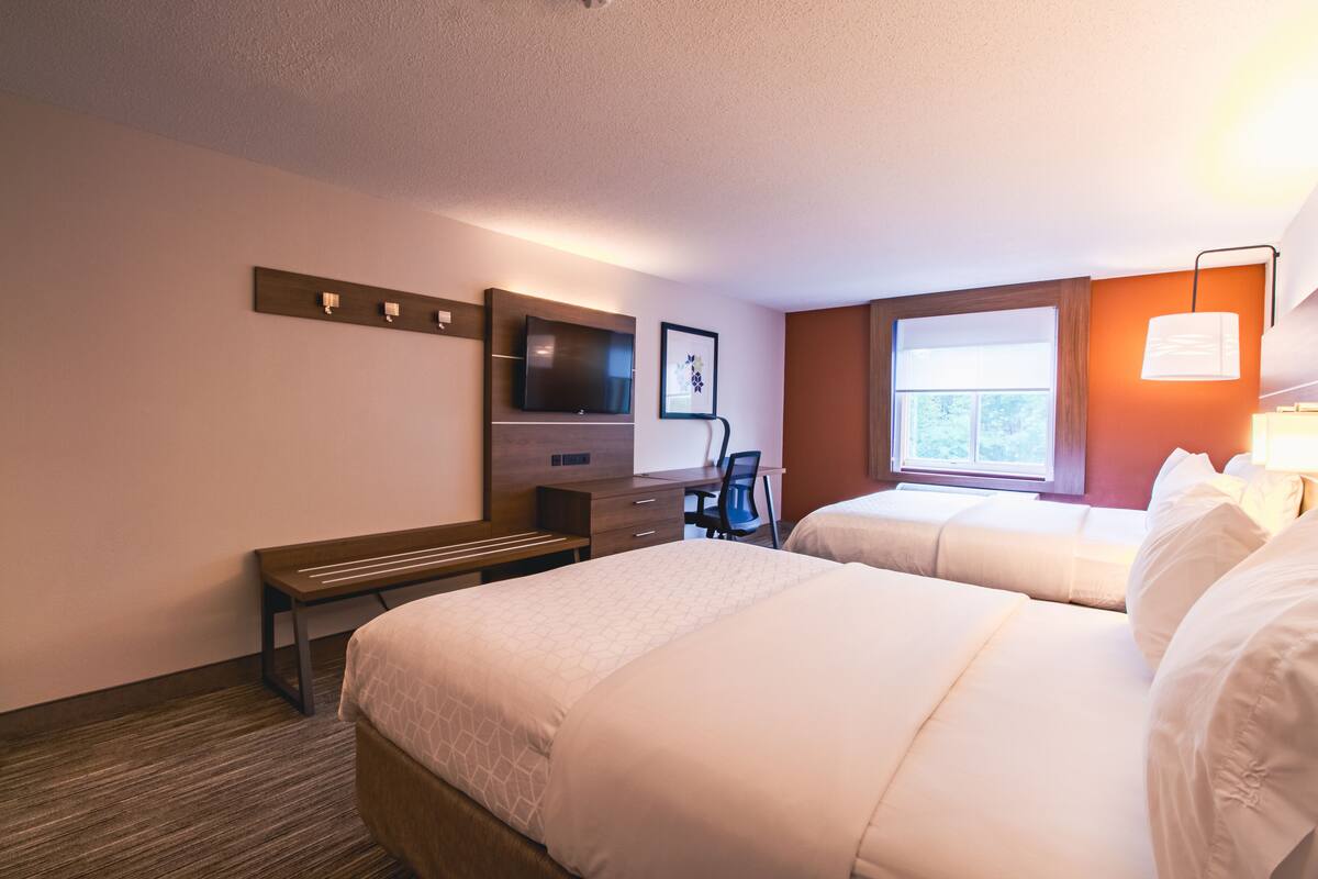 Ein Hotelzimmer mit zwei Betten, einem Schreibtisch, einem Sessel, einem Fernseher und einem Fenster.