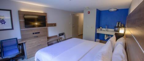 A hotel room with a large bed, a desk with a chair, a TV mounted on the wall, and a bathroom with a mirror and sink.