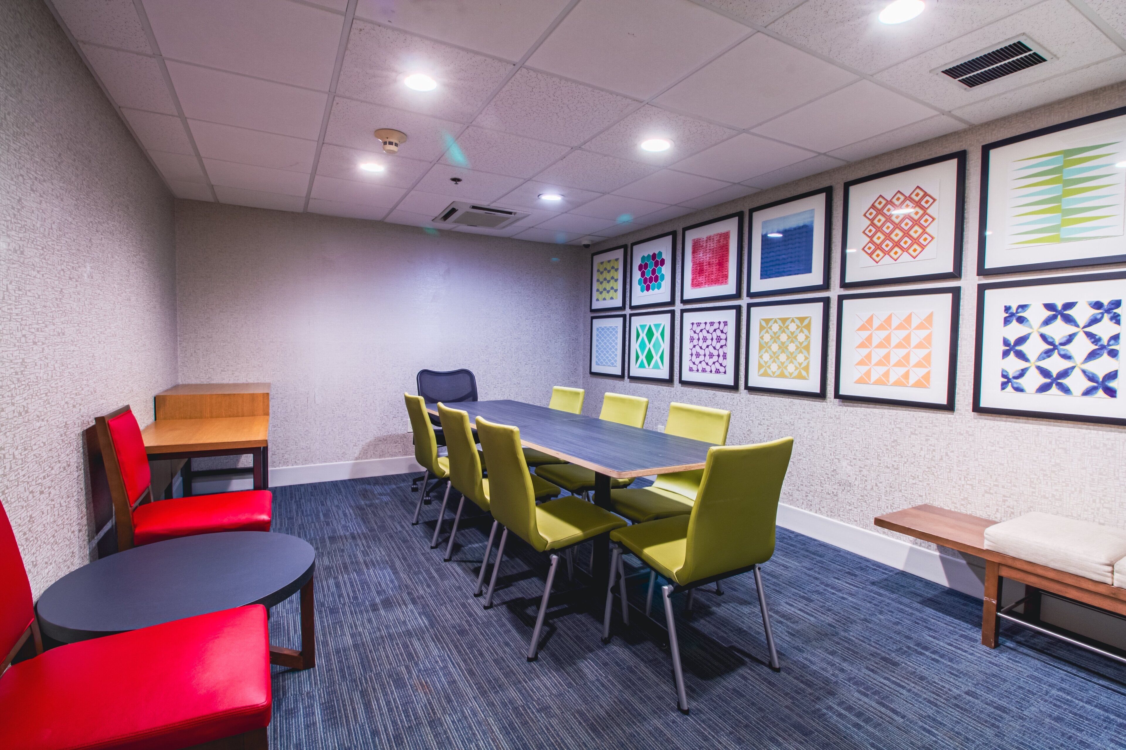 A conference room with a long table, yellow chairs, and red chairs. There are framed patterns on the wall.