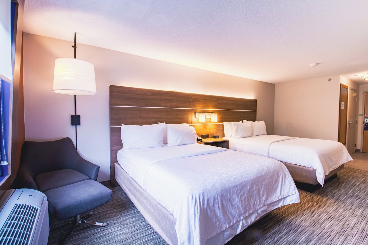 A hotel room with two beds, a chair, a desk, and a lamp.