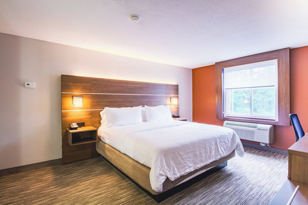 A hotel room with a large bed, bedside tables, a desk, and a window with a view.