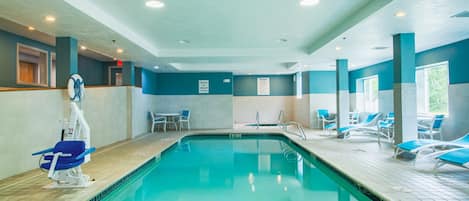 An indoor swimming pool with a blue and white color scheme, a lifeguard chair, and lounge chairs around the pool.