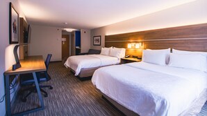 Habitació d'hotel amb dos llits, un escriptori amb una cadira, una tauleta de nit amb una làmpada i un quadre encimbellat a la paret.