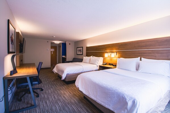 A hotel room with two beds, a desk with a chair, a nightstand with a lamp, and a framed picture on the wall.