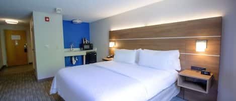 Habitación de hotel con una cama grande, una mesita de noche con un reloj, un buró, un escritorio con una computadora y una pared azul decorativa.
