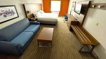A hotel room with a bed, a blue sofa, a wooden bench, a small table, a TV, and a framed picture on the wall.