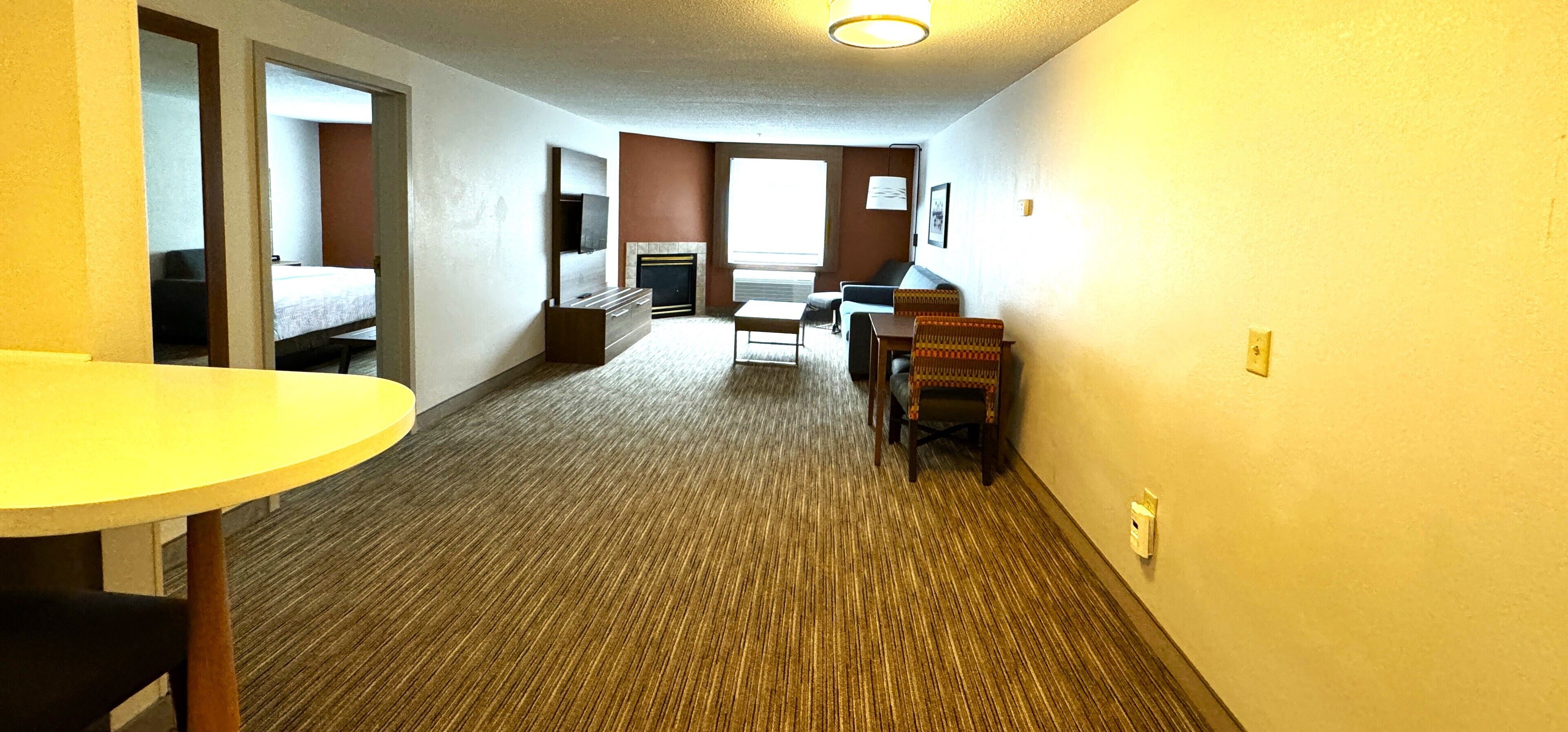 A hotel room with a bed, a desk, a chair, a small table, and a fireplace.