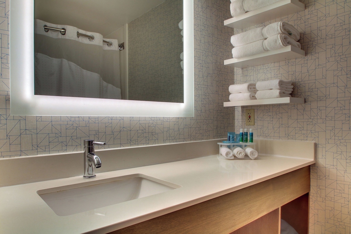 A bathroom with a sink, mirror, towel racks, and a geometric patterned wall.