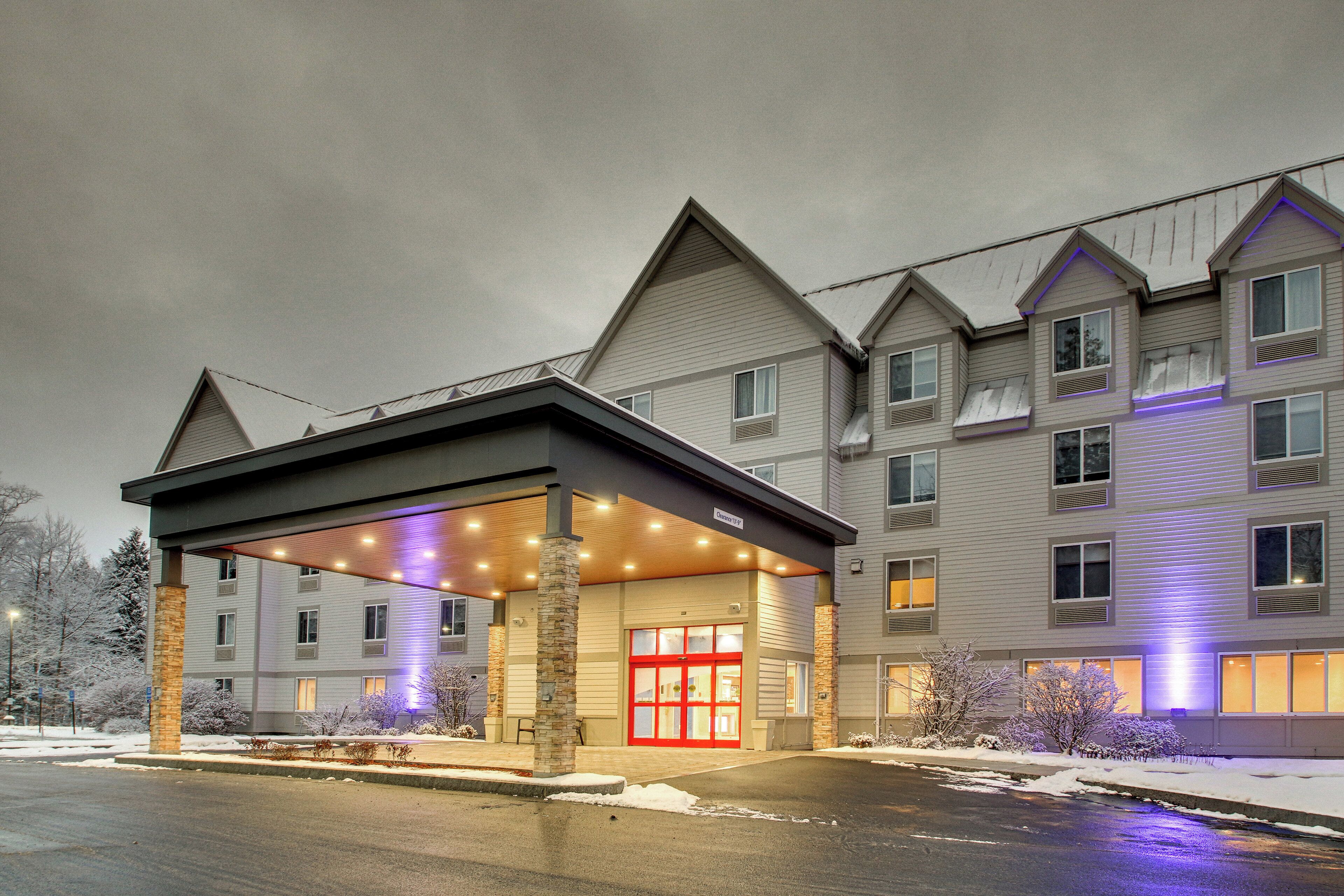 A multi-story hotel with a covered entrance and a red door, featuring a stone pillar and a parking lot with snow.