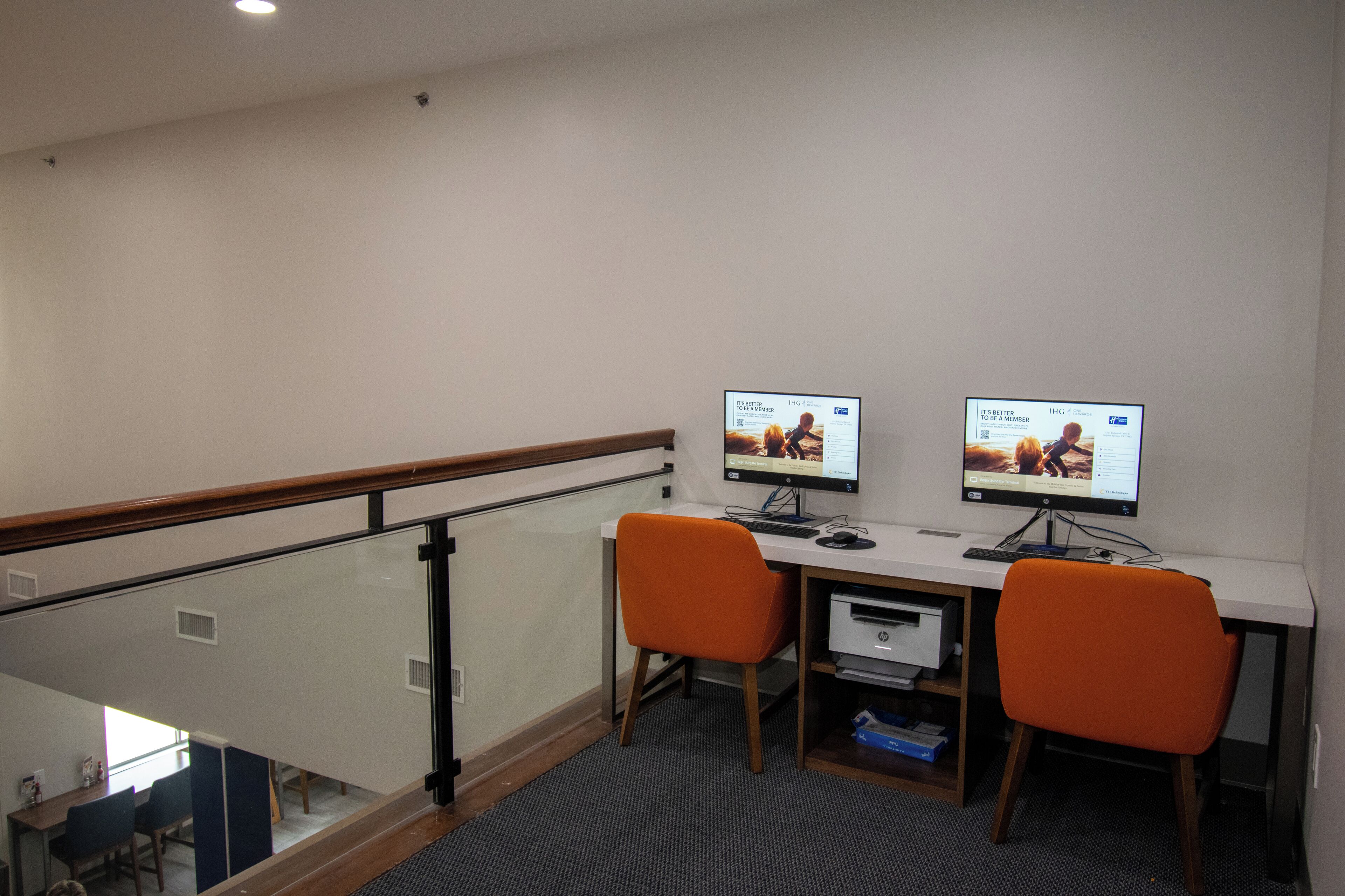 Un espace de bureau moderne comprenant deux bureaux, chacun équipé d’un écran d’ordinateur, d’une chaise orange et d’une imprimante.