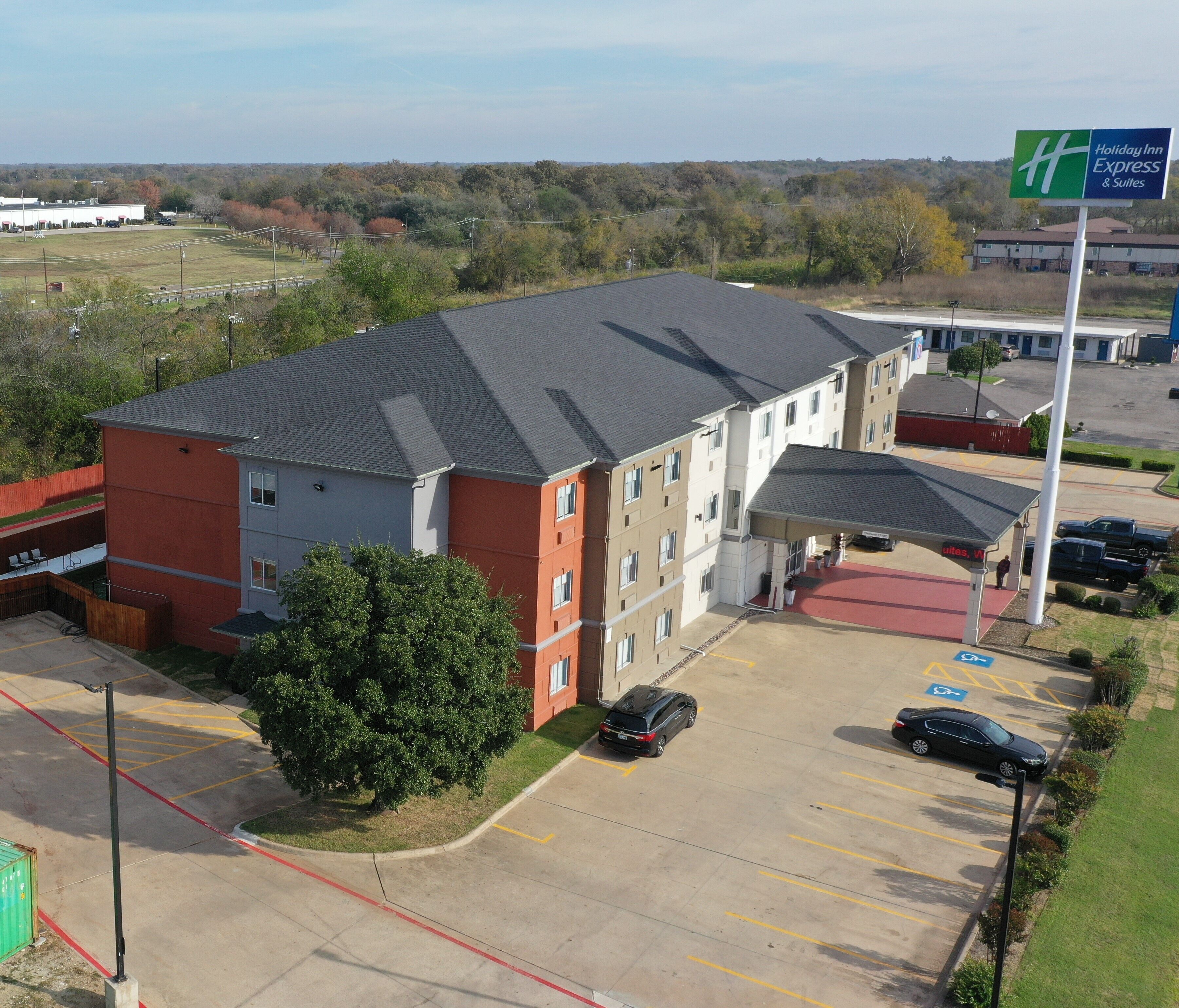 A Holiday Inn Express & Suites with a parking lot, a covered outdoor area, and a view of the surrounding landscape.