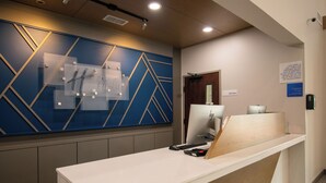 A hotel reception desk with a modern design, including a blue geometric wall panel and a wooden counter. - Holiday Inn Express and Suites Sulphur Springs by IHG (Sulphur Springs)