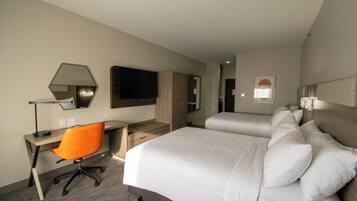 Een hotelkamer met een bureau, een oranje bureaustoel, twee bedden met witte lakens, een grote spiegel en een flatscreen televisie.