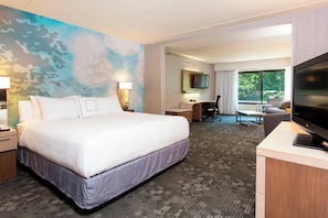 A hotel room with a large bed, a desk, a chair, a TV, and a window with a view of greenery. - Courtyard Marriott Binghamton (Vestal)