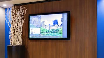 A hotel reception area with a large screen displaying a cityscape, a potted plant, and a wooden reception desk.