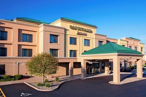 A Courtyard by Marriott hotel with a green-roofed entrance pavilion, a landscaped area with a small tree, and a clear blue sky. - Courtyard Marriott Binghamton (Vestal)