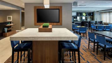 Una hall moderna di un hotel con un grande televisore a schermo piatto montato a parete, un’area bar con sedute blu e una moquette decorata.