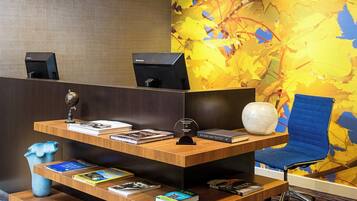 A reception desk with a computer, a blue chair, and a decorative wall with abstract patterns.